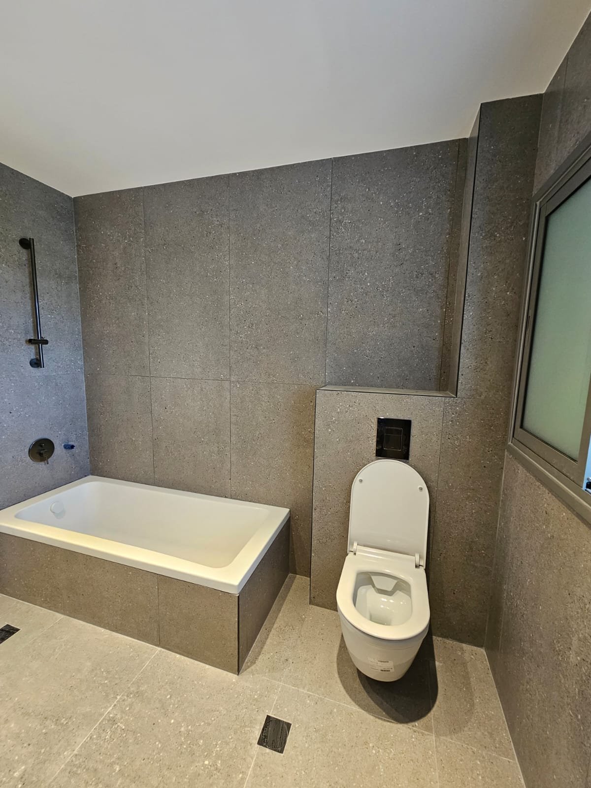 שיפוץ חדר רחצה מודרני עם אמבטיה מובנית וחיפוי אפור מונוליטי