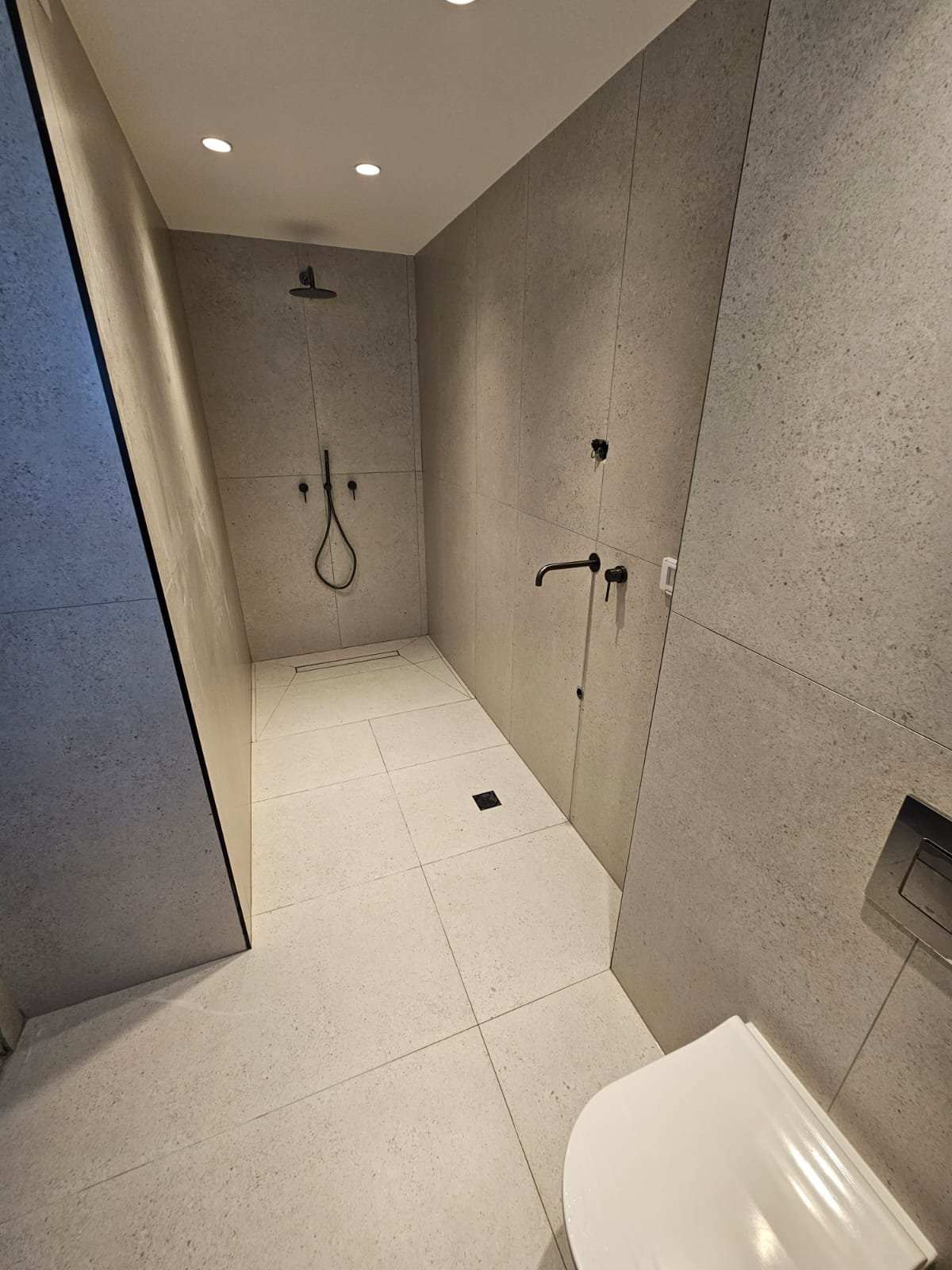 מקלחת Walk-In מודרנית עם חיפוי אפור רציף וברזים שחורים