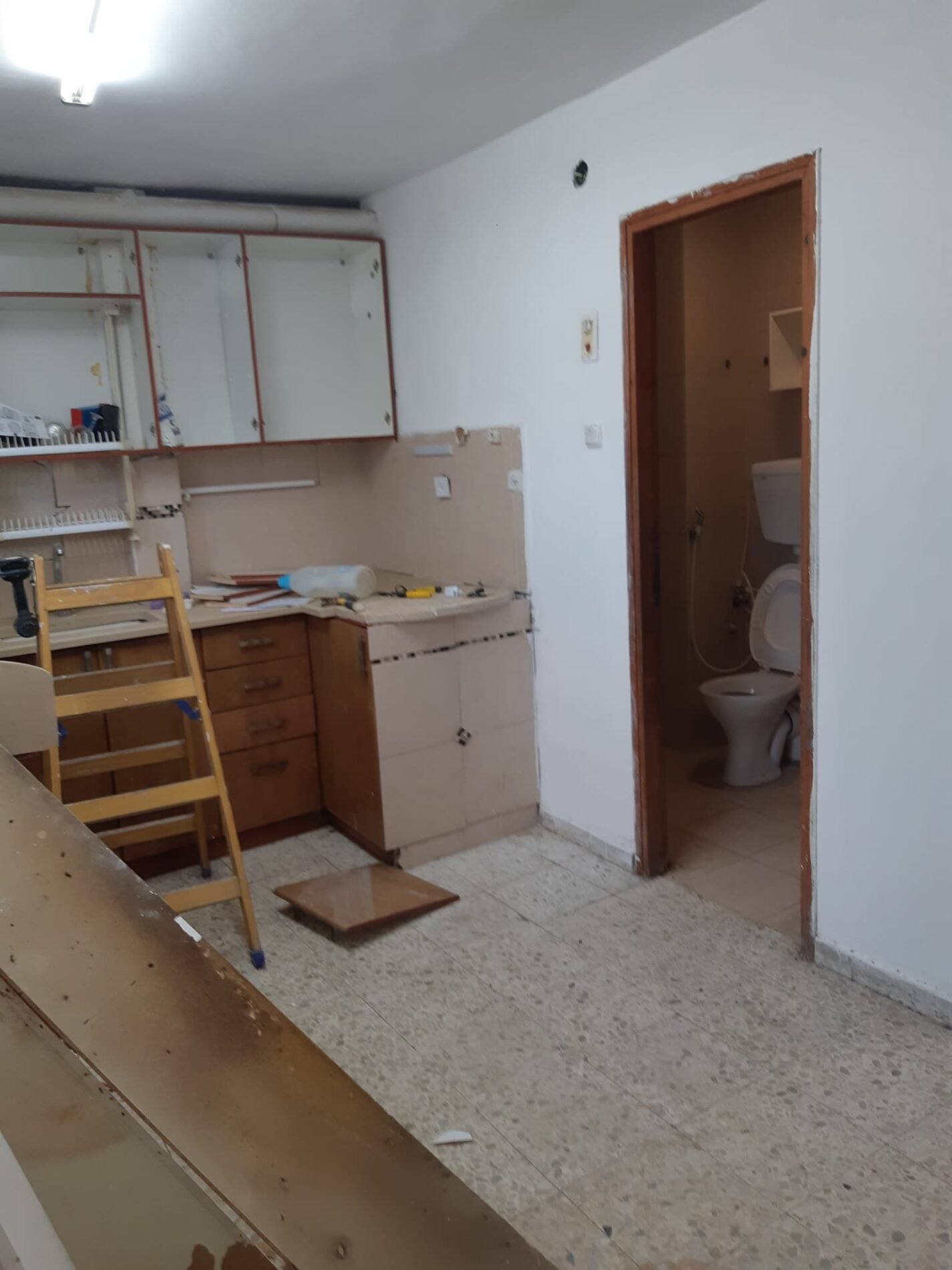 מטבח קטן לפני שיפוץ עם חלון צר ודלת לחדר הרחצה